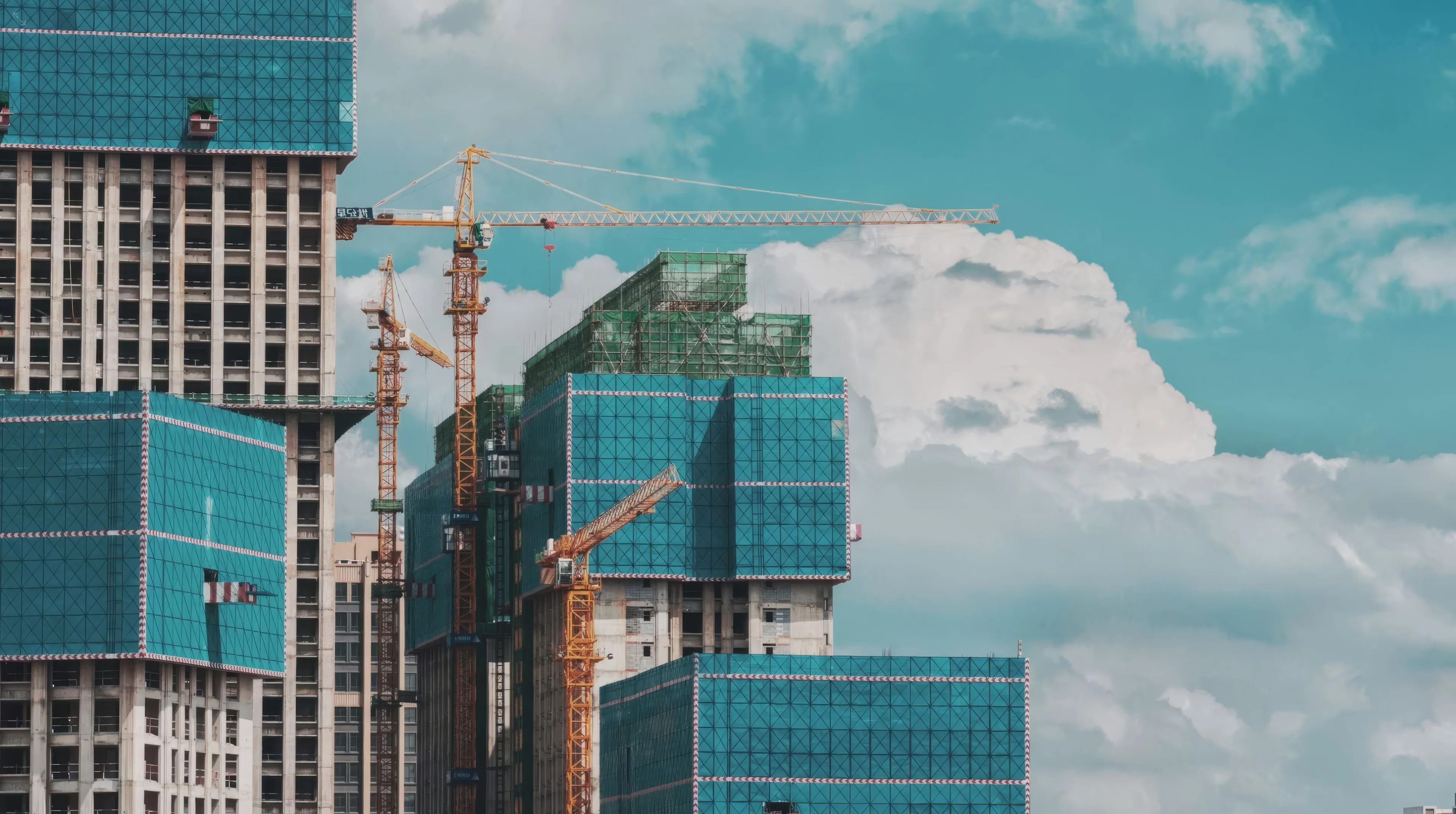 Towers under construction with cranes against a blue sky.