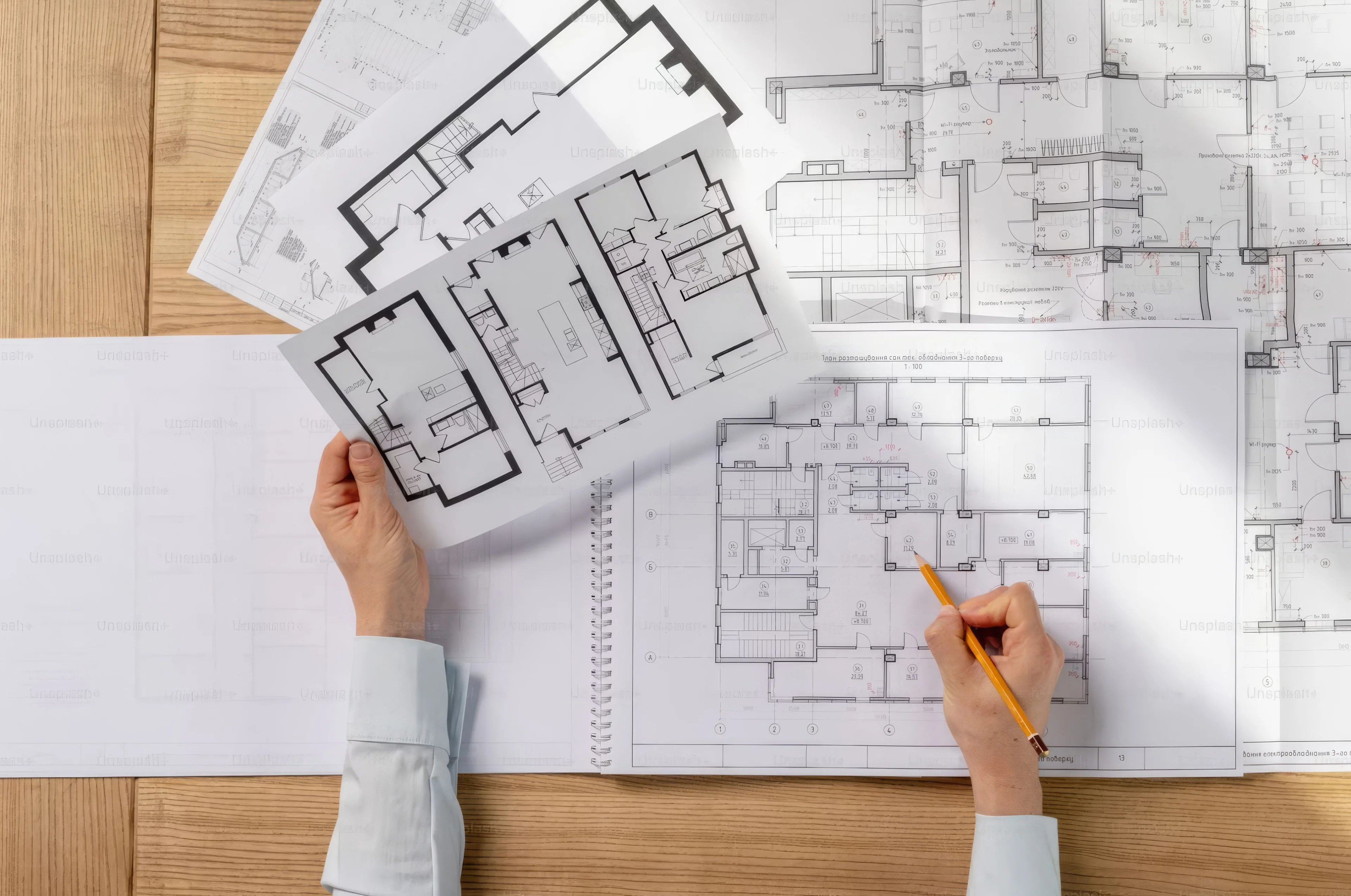 Floor plans spread on a desk, with a hand holding a pencil.