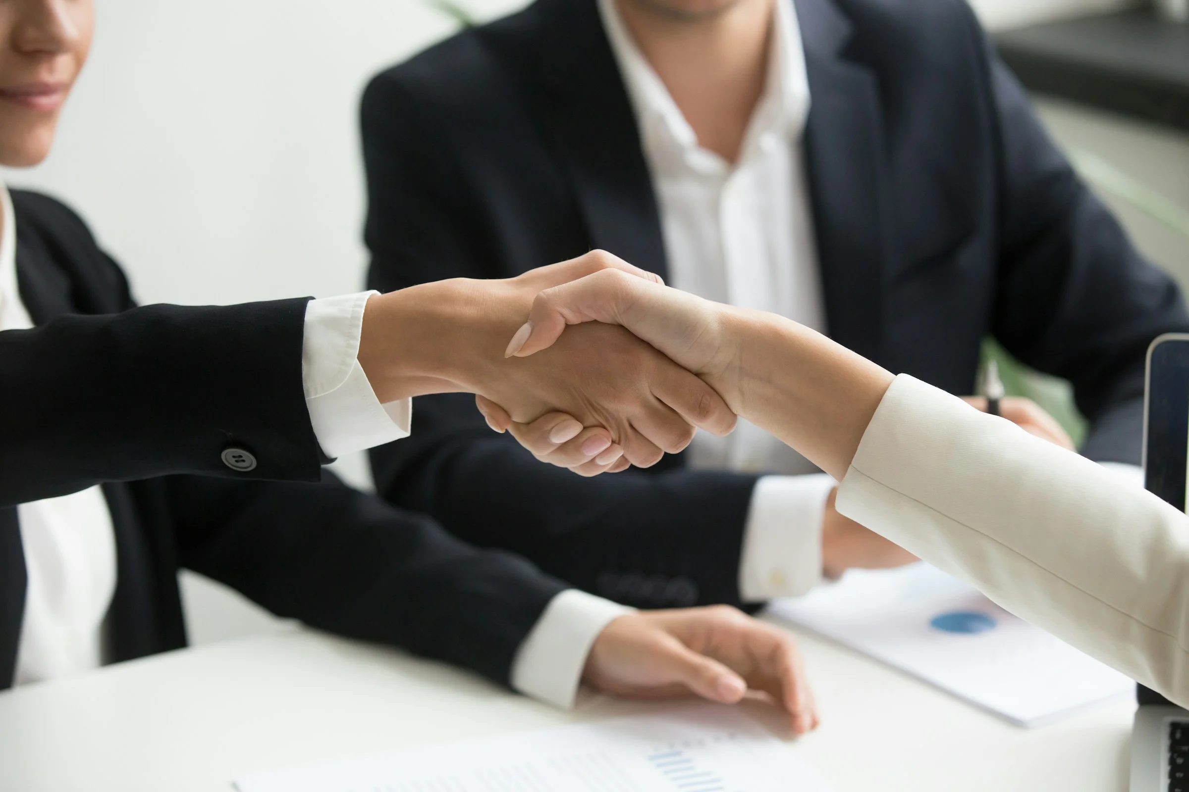 Two people shaking hands across a table.