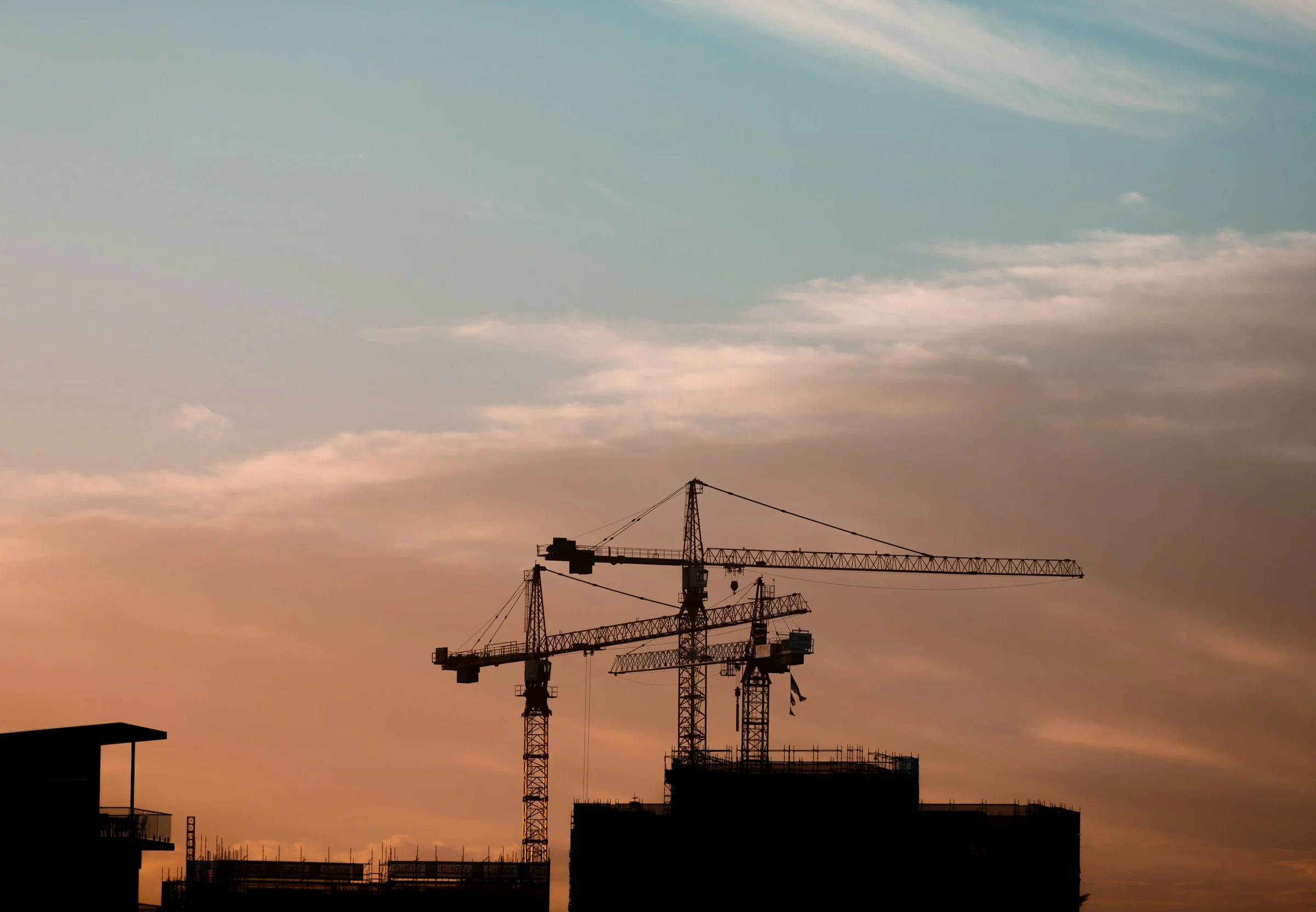 Three tower cranes against a sunset sky.